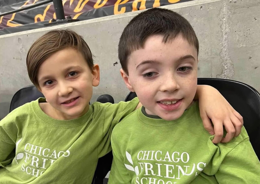 Two friends wearing school t-shirts sitting next to each other, one with his arm around the other